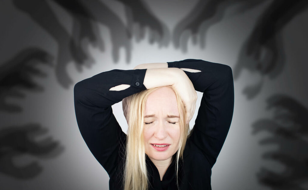 Woman overwhelmed by anxious thoughts as shadowy hands reach out for her representing someone who could benefit from ADHD-Focused Therapy for Anxiety in NYC.