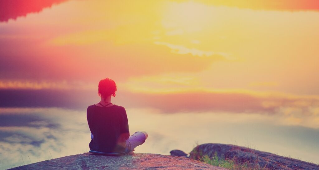 Young woman sitting on a rock outcropping representing someone who found peace through ADHD-Focused Therapy for Anxiety in NYC.