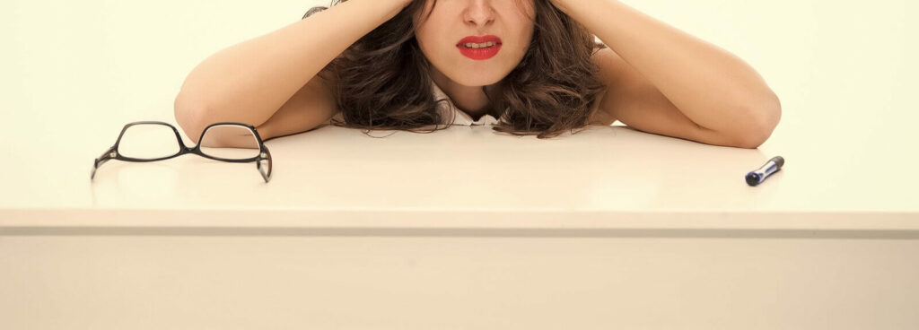 stressed woman - ADHD Focused Therapy in NYC - therapy for ADHD - ADHD focused therapy for couples - 10018 - 10010 - 10003 - 10011 Woman with her head on her desk as she struggles to manage her ADHD at work representing someone who would benefit from the skills gained though ADHD Focused Therapy in NYC.